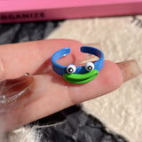 Bague moche, monstre-grenouille bleu avec une grosse bouche verte souriante et de grands yeux ronds.
