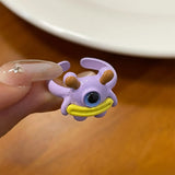 Bague créature violette avec un œil bleu, une large bouche jaune et des cornes marrons.