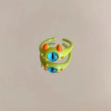 Bague créature verte avec un œil bleu, des tâches orange et deux cornes orange.