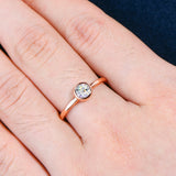 Une main portant une bague couleur or rose avec une moissanite sertie clos.