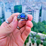 Une main d'homme tenant une bague pour homme  avec une pierre centrale bleue.