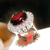 Bague rubis ancienne avec une zircone rouge ronde entourée d'un halo de zircons, posée sur son écrin blanc.