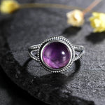 Bague améthyste en argent avec un anneau texturé, posée sur une pierre  plate noire.