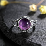 Bague améthyste en argent avec un anneau texturé, posée sur une pierre  plate noire.