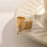 Bague avec breloque perle en acier de couleur dorée, posée sur une sous-tasse.