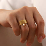 Main de femme portant une bague avec breloque perle blanche sur son annulaire.