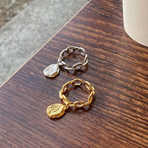 Bague avec pendentif de couleur argent, et une autre de couleur or, posées sur une table en bois.