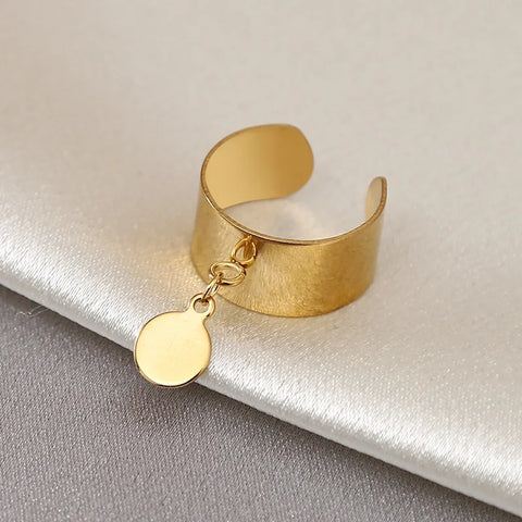Bague breloque dorée avec une petite médaille ronde suspendue.