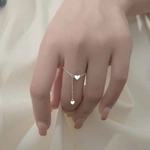 Bague chaînette argentée avec un anneau fin et 2 pendentifs coeurs, portée sur le majeur d'une femme.