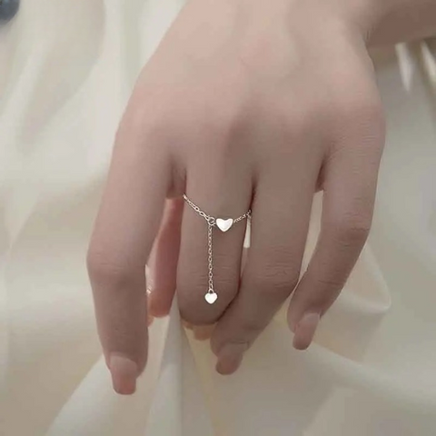 Bague chaînette argentée avec un anneau fin et 2 pendentifs coeurs, portée sur le majeur d'une femme.