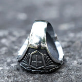 Bague chevalière couleur argentée, avec des motifs croix sur les côtés et un anneau lisse à l'arrière.