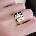 Main portant une bague chevalière homme couleur or avec une grande pierre ronde au centre et petites pierres.