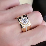 Main portant une bague chevalière homme couleur or avec une grande pierre ronde au centre et petites pierres.