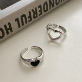 Bague cœur à pendentif creux posé à côté d'une bague coeur avec pierre noire.