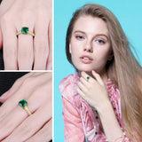 Bague de fiançailles émeraude en argent doré avec une émeraude verte, portée sur le majeur d'une femme.