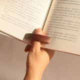 Femme tenant les pages d'un livre en place avec sa bague de lecture en bois.