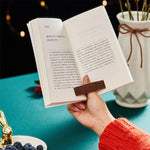 Femme tenant son livre en place grâce à la bague de lecture marron en bois qu'elle porte à son doigt.