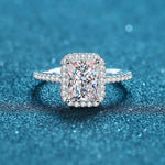 Bague de mariage de luxe avec une grande pierre carrée entourée de petites pierres posée sur une table.