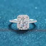 Bague de mariage de luxe avec une grande pierre carrée entourée de petites pierres posée sur une table.