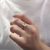 Bague demande en mariage en argent doré avec une pierre rectangulaire portée sur le majeur d'une femme.