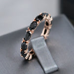 Bague diamant noir avec un anneau rose gold décoré de zircones noirs ovales sur tout le tour, posé dans un écrin gris.