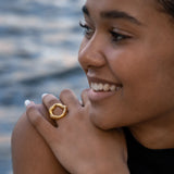 Bague dorée en acier inoxydable portée sur l'annulaire d'une femme, posant sa main sur son épaule.