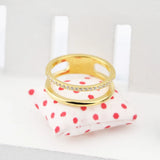 Bague double anneau en acier inoxydable de couleur dorée, posée sur un petit coussin.