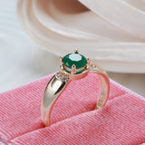 Bague emeraude or rose 585 avec des griffes, une zircone verte et de petites pierres, posée dans un écrin rose.