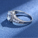 Bague de fiançailles diamant en argent avec un gros zircone central entouré de petits diamants ronds, posée sur une table.
