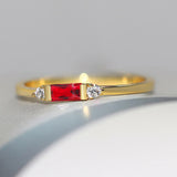 Bague fine couleur dorée avec une zircone rectangle rouge et deux petites pierres rondes sur les côtés.