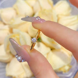 Bague fine or jaune 18 carats solitaire tenue entre les deux doigts d'une femme.