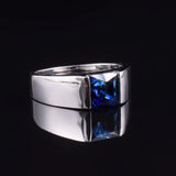 Bague homme saphir en argent avec un saphir carré, posée sur une table noire.