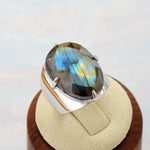Bague labradorite avec anneau en cuivre et grande pierre ovale, posée sur un écru beige.