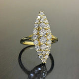 Bague marquise dorée pavée de zircones cubiques, posée sur une surface sombre et réfléchissante.