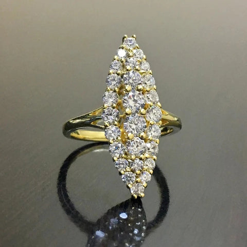 Bague marquise dorée pavée de zircones cubiques, posée sur une surface sombre et réfléchissante.
