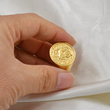 Bague Napoléon dorée avec un motif de pièce de monnaie au centre tenue par une main.