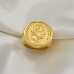 Bague Napoléon dorée avec un motif de pièce de monnaie posée sur un tissu délicat.