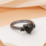 Bague noire femme avec un anneau noir en alliage et une pierre coeur noire, posée sur une table.