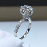 Bague couleur or blanc diamant, avec une moissanite ronde sertie de griffes et un anneau pavé de petites pierres.