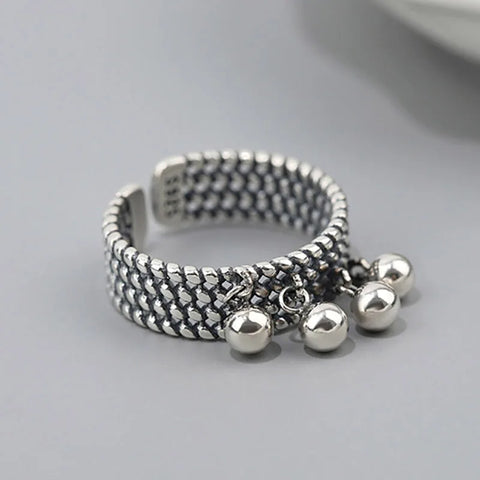 Bague pendentif avec une large bande à motif de mailles et quatre pendentifs en forme de billes.