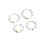 4 bagues perlée en perles blanches de tailles différentes posée sur une surface blanche.