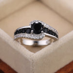 Bague pierre de couleur argent, avec une pierre ovale noire et des rangées de petites pierres noires et blanches.