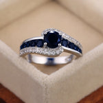 Bague pierre de couleur argent, avec une pierre ronde bleue et des rangées de petites pierres bleues et blanches.