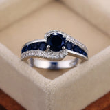 Bague pierre de couleur argent, avec une pierre ronde bleue et des rangées de petites pierres bleues et blanches.