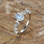 Bague pierre de lune sur un fond naturel et rustique, avec des motifs de lunes et d'étoiles incrustés de pierres.