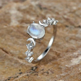 Bague pierre de lune sur un fond naturel et rustique, avec des motifs de lunes et d'étoiles incrustés de pierres.