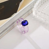 Bague plastique violet en résine avec une pierre rectangle bleue.