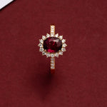 Bague rubis couleur or avec un anneau fin, posée sur une boîte rouge.