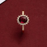 Bague rubis couleur or avec un anneau fin, posée sur une boîte rouge.
