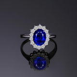 Bague saphir bleu avec un saphir bleu ovale et des zircones tout autour, posée sur une table.